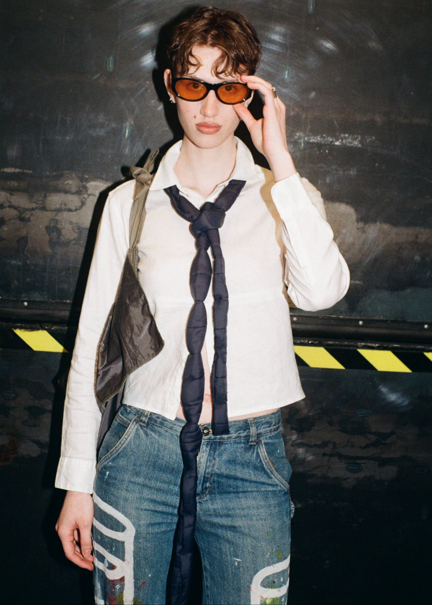 Person wearing sunglasses and a white shirt with a dark tie against a dark background