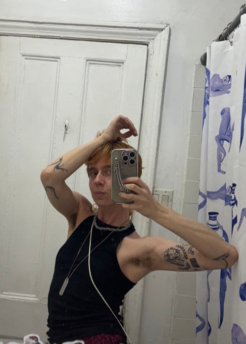 Person taking a mirror selfie in a bathroom with a shower curtain in the background.