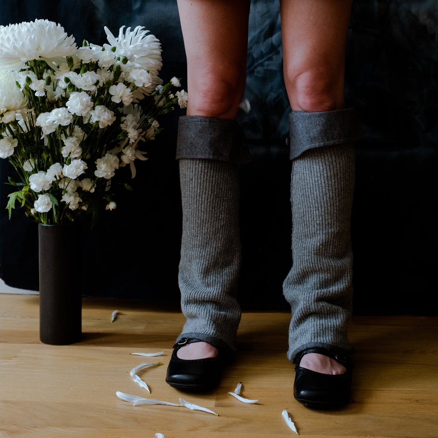 lower legs of a model wearing gray knit leg warmers with gray cuffed tops standing next to a pot of white flowers