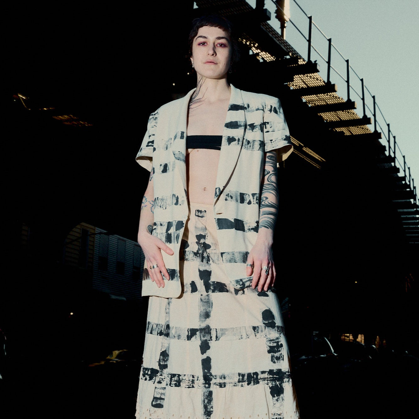 Person wearing a patterned outfit standing on a staircase at night.