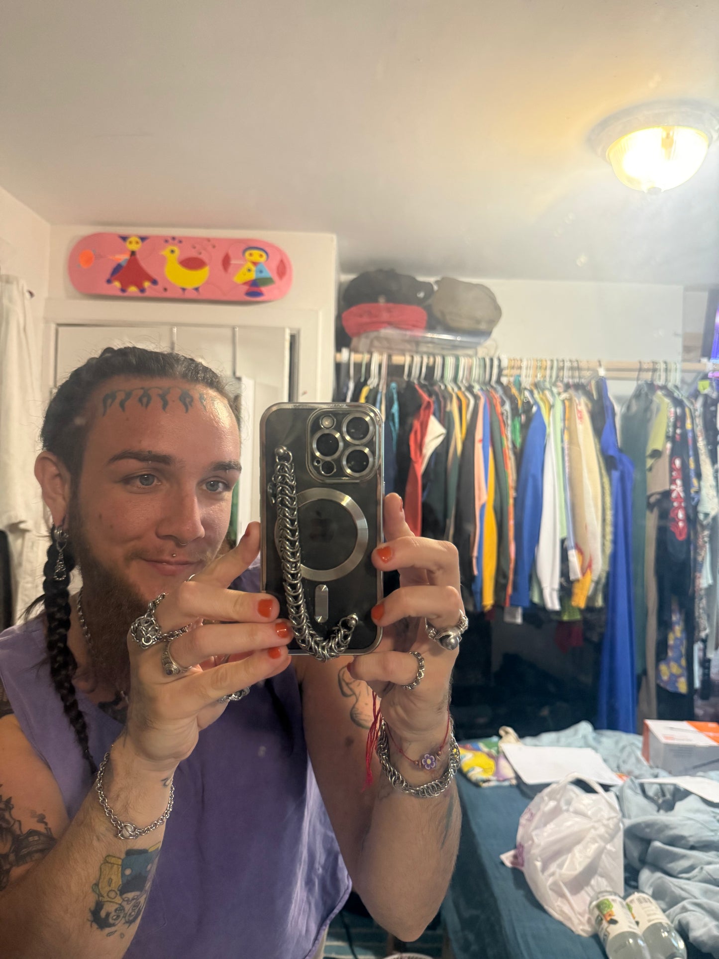 Person taking a mirror selfie in a room with clothing racks and a colorful skateboard.
