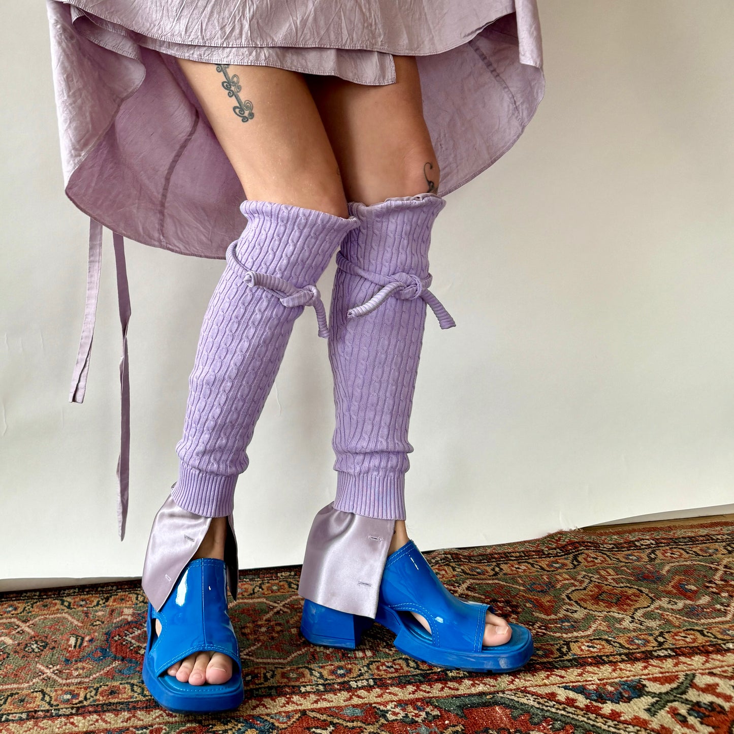 purple cable knit leg warmers with silk purple cuffs at the bottom and cable knit ties at the top worn by a model wearing bright blue shoes