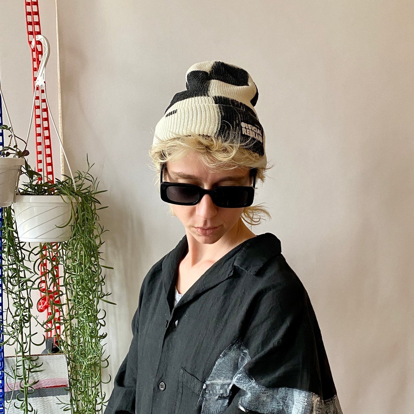 Model wearing cream beanie with hand painted black checkered squares and a black tag with white text reading OFFICIAL REBRAND on the hat's cuff