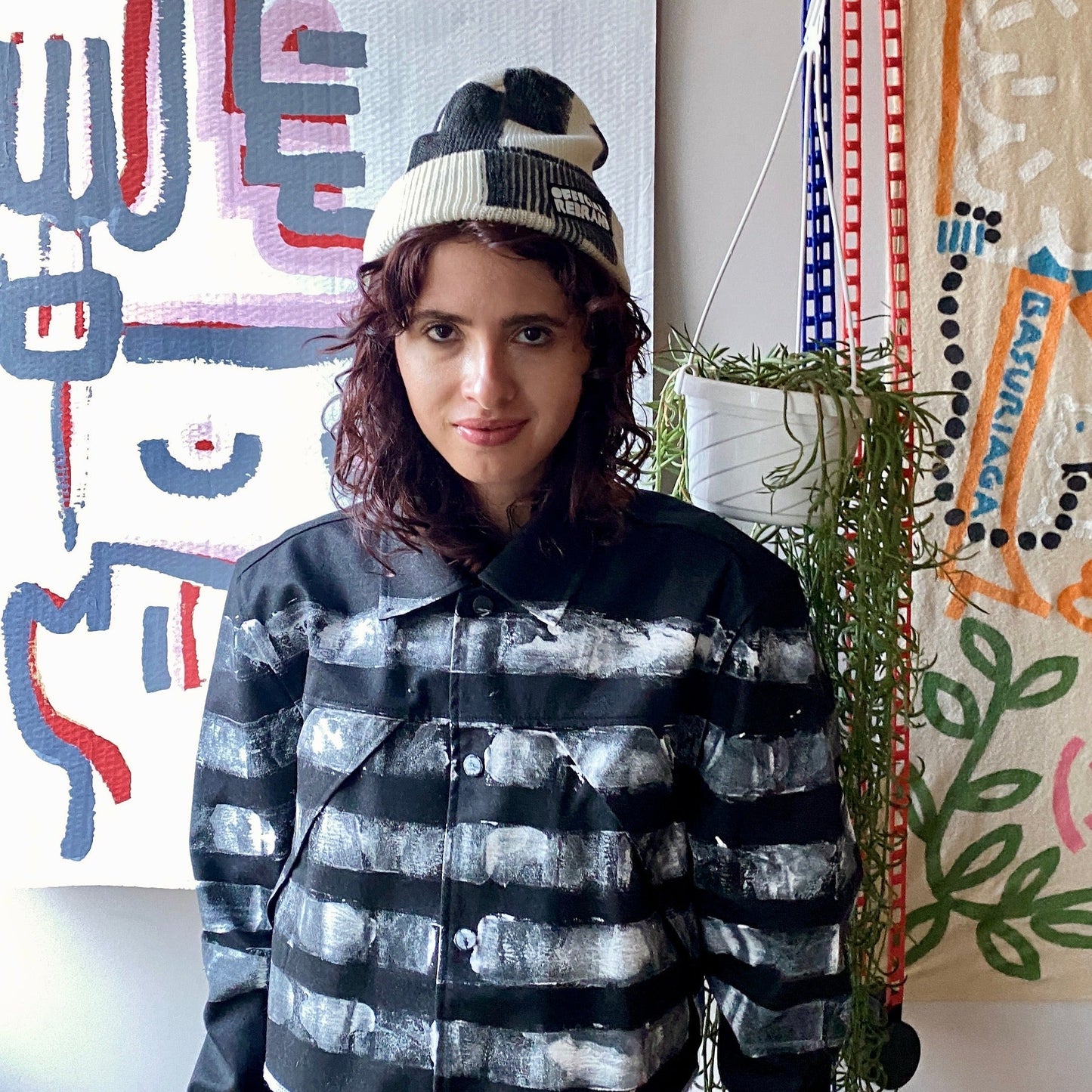 Model wearing cream beanie with hand painted black checkered squares and a black tag with white text reading OFFICIAL REBRAND on the hat's cuff