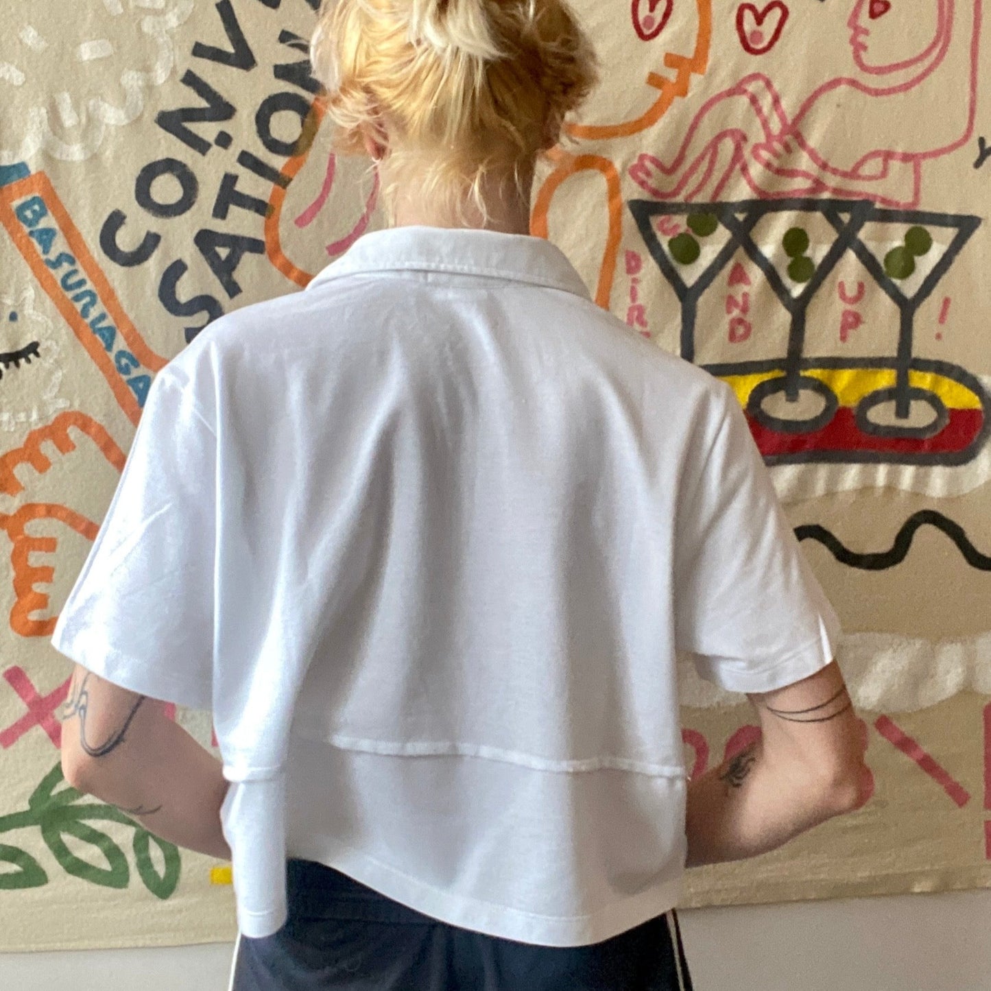 model wearing white cropped polo shirt facing away to show the back