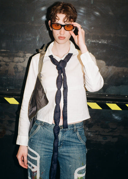 Person wearing sunglasses and a white shirt with a dark tie against a dark background