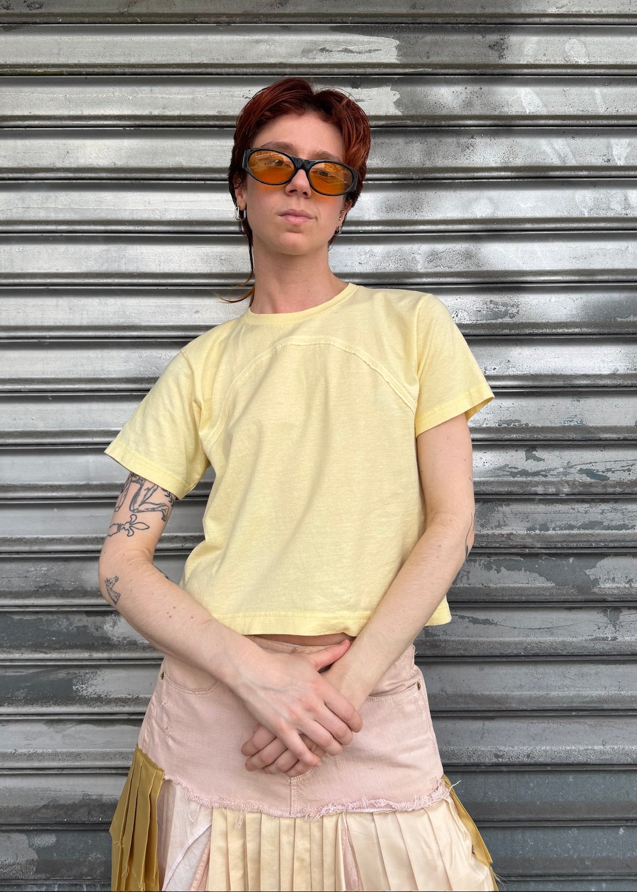 Person wearing a yellow shirt and sunglasses standing in front of a metallic shutter.