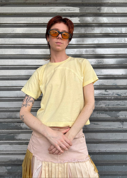 Person wearing a yellow shirt and sunglasses standing in front of a metallic shutter.