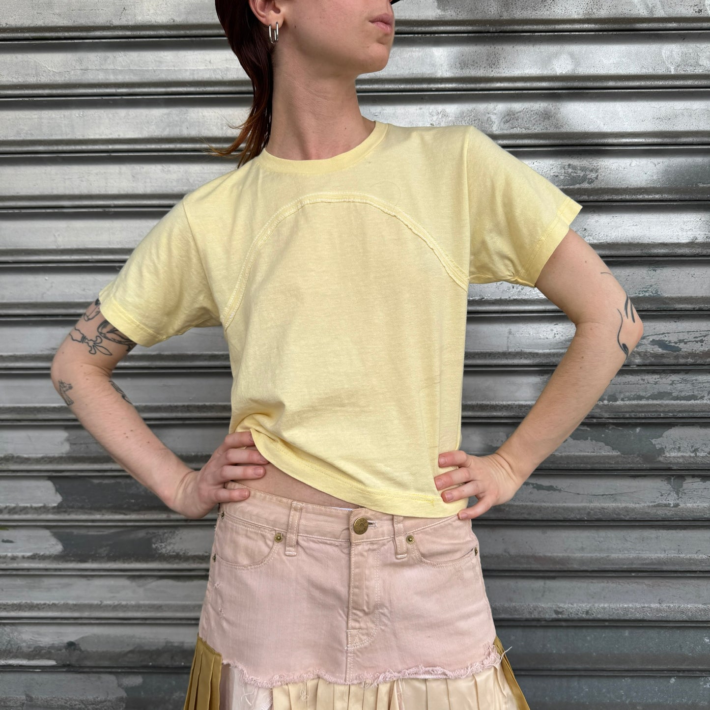 Person wearing a yellow crop top and pink skirt against a metallic shutter background