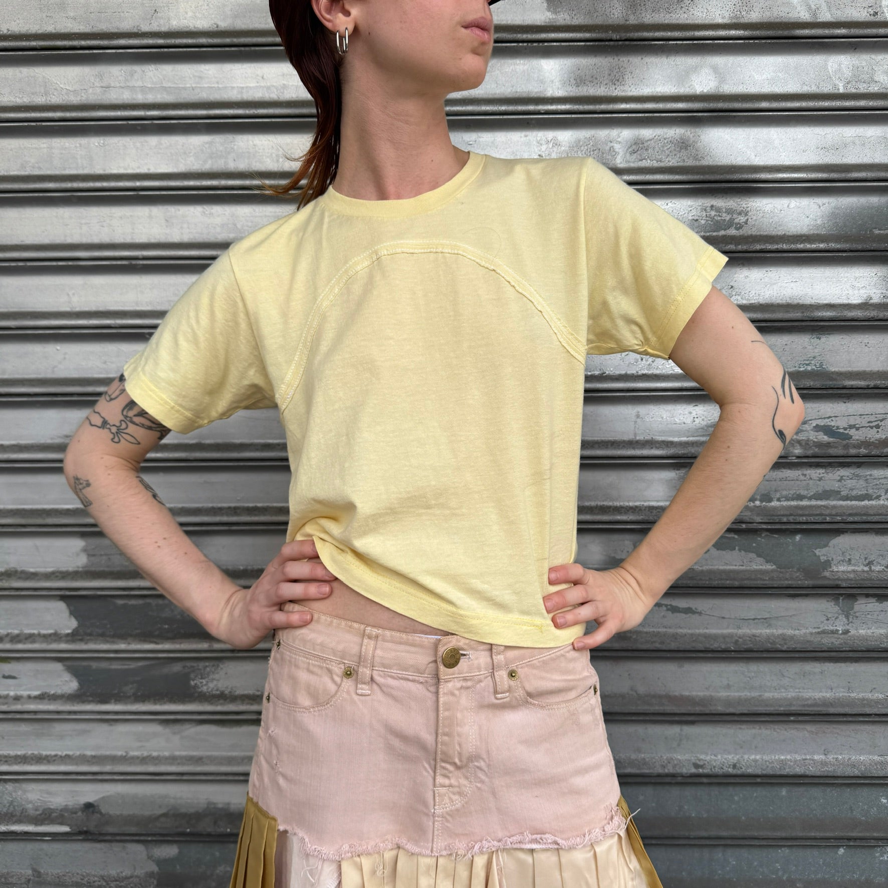 Person wearing a yellow crop top and pink skirt against a metallic shutter background