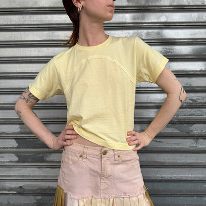 Person wearing a yellow crop top and pink skirt against a metallic shutter background