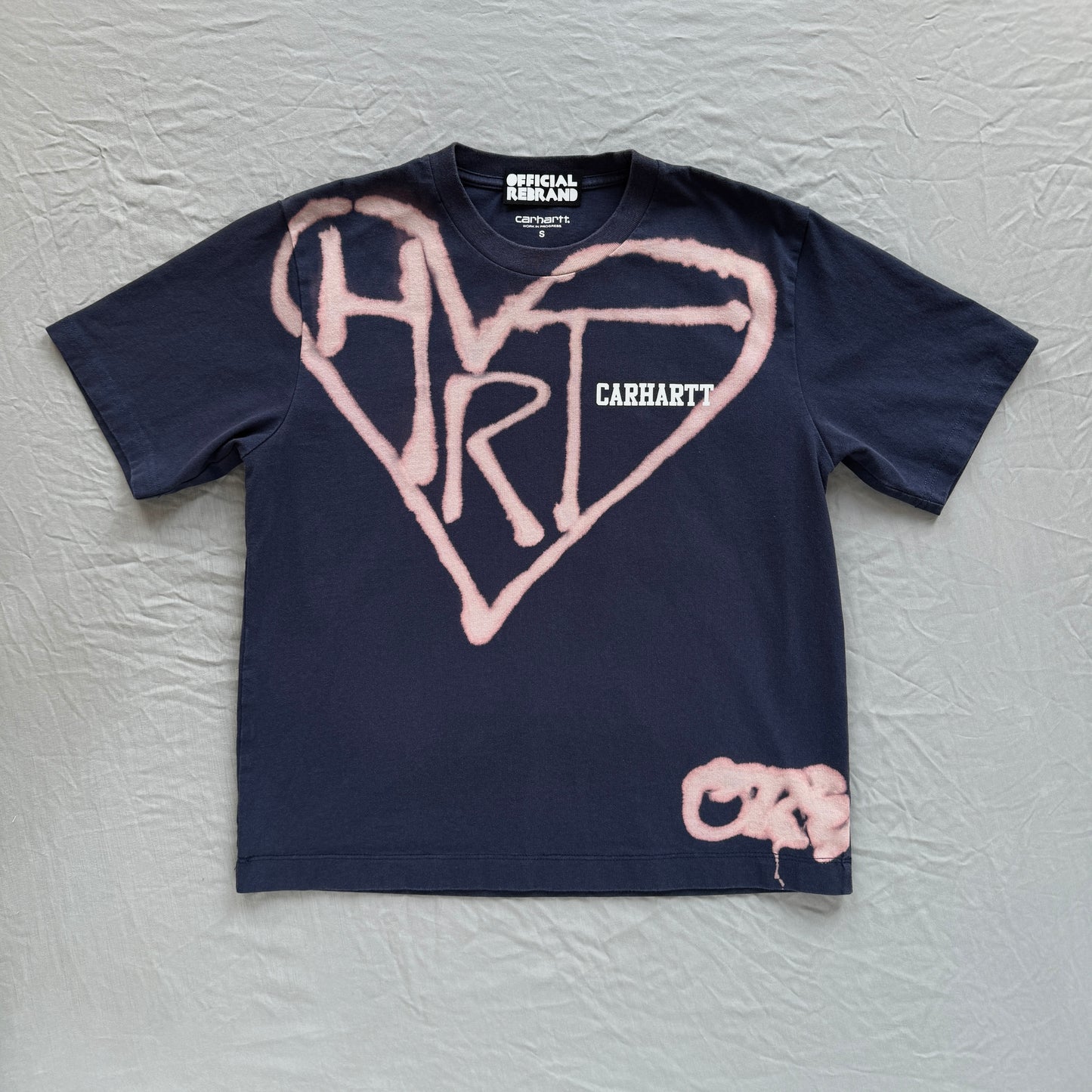 Navy carhartt Tee with printed Carhartt text on upper right chest in white block letters  on gray background with bleach heart and bleach text reading HRT.