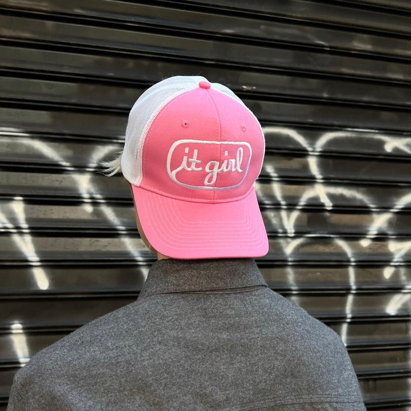 model facing away wearing pink and white trucker hat with white embroidery reading it girl in cursive