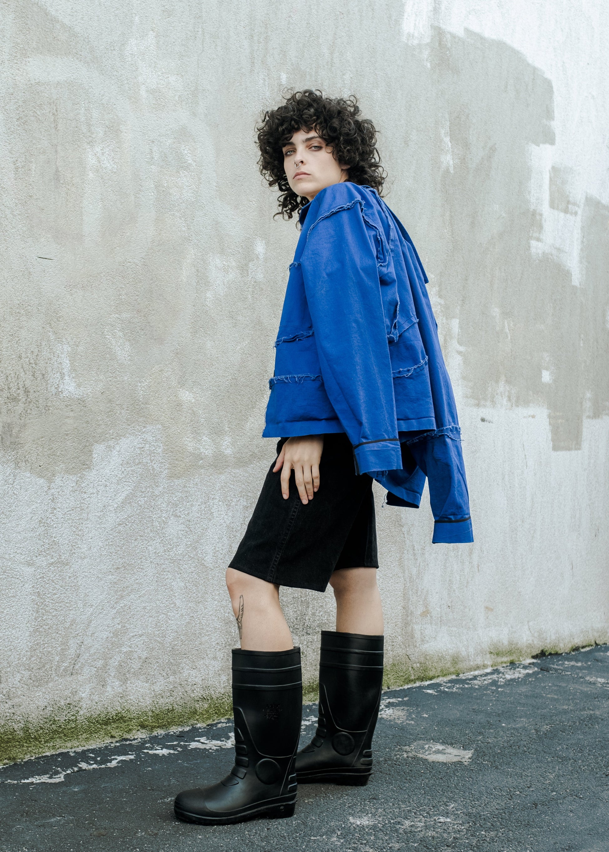 model turned to the side wearing cobalt blue jacket draped over shoulders and black boots