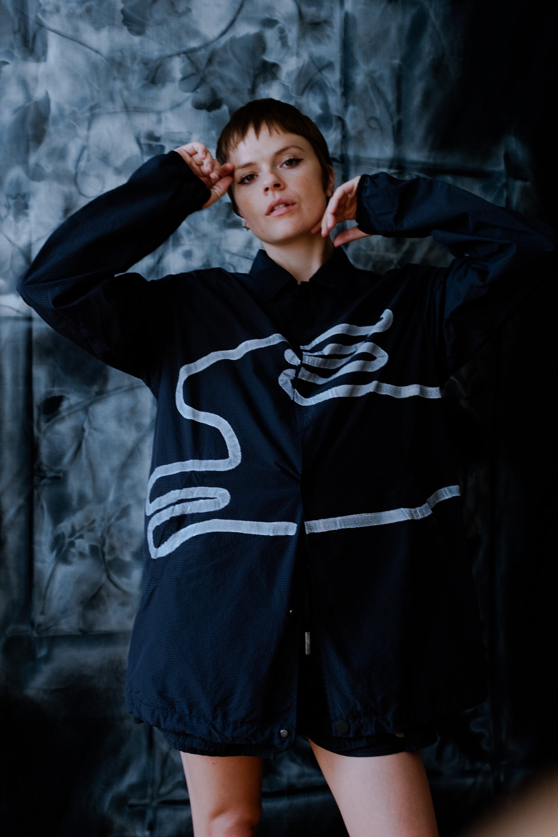 Model posing wearing navy blue seersucker collared windbreaker with hand painted white rabbit silhouette across front