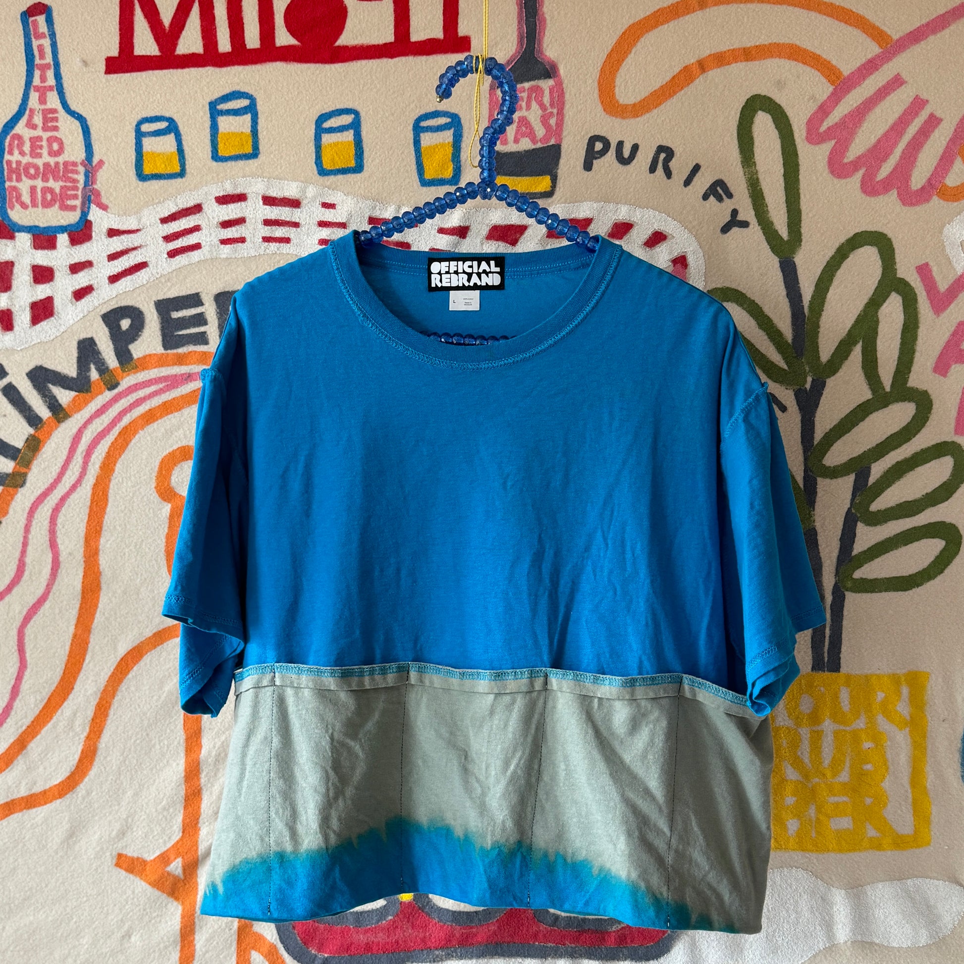 bright blue tshirt with folded pockets along the bottom. Pockets are color stripped to be a light mossy green