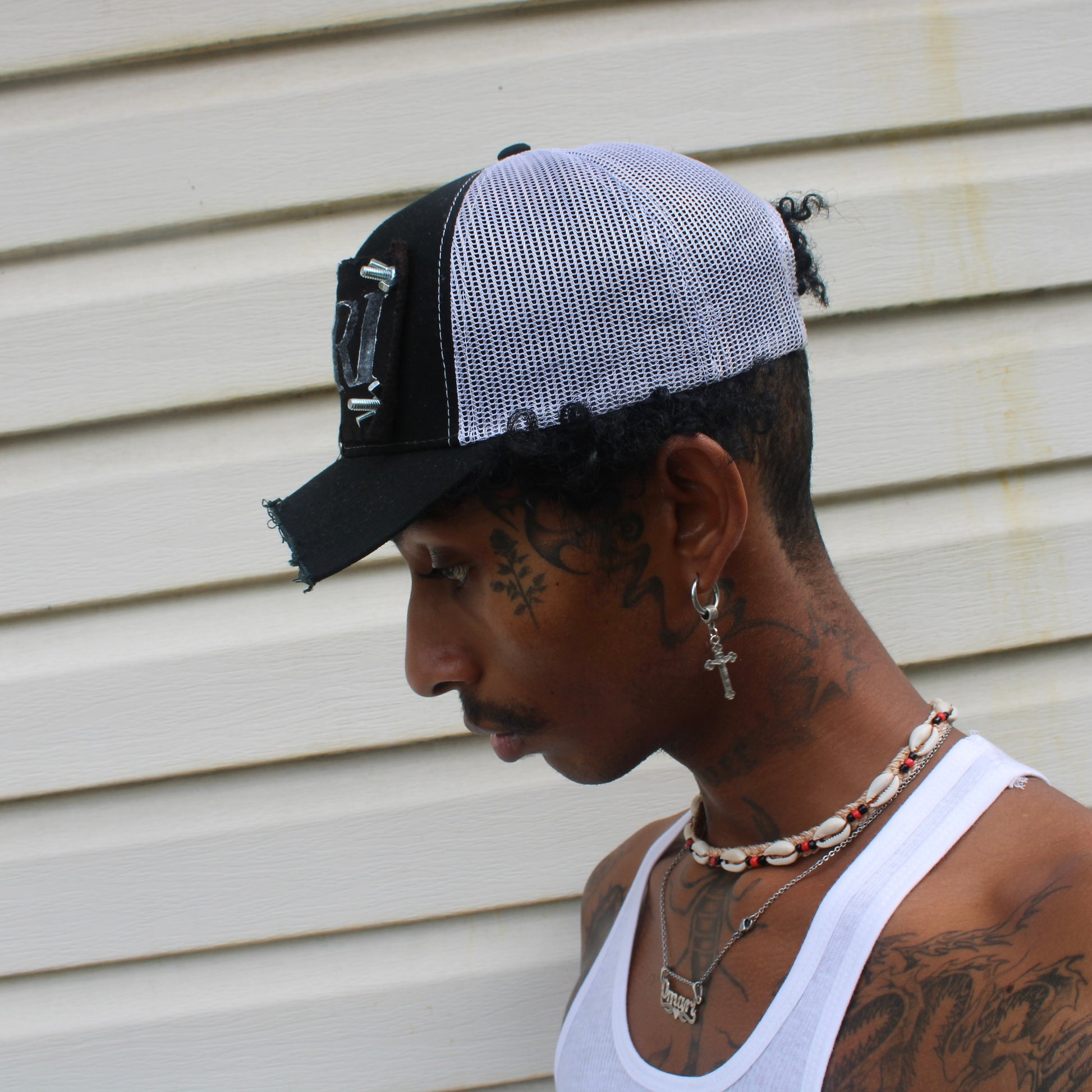 profile of model wearing chopped brim trucker hat with white mesh back, black patch with white INRI stamp, and nuts and bolts affixing the four corners of the patch to the front of the hat