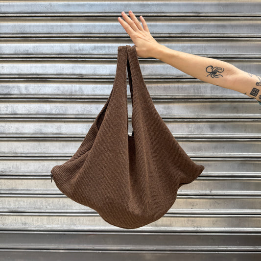 Brown knit bag held by a hand against a metallic background