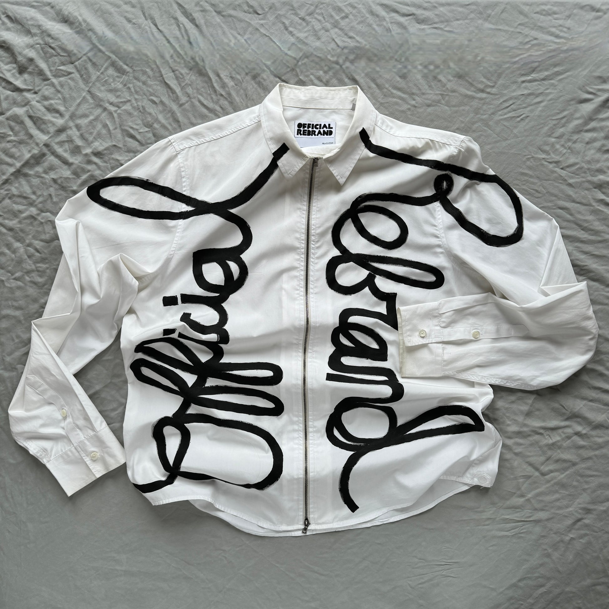 white zippered collared shirt with official rebrand hand painted in black across the front in cursive