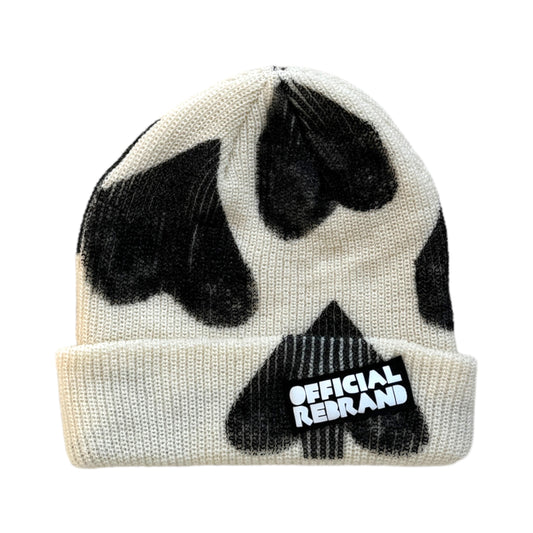 cream wool beanie with hand painted black hearts and a black tag with white text reading OFFICIAL REBRAND on the hat's cuff