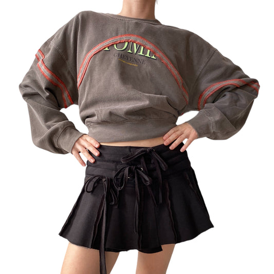 figure wearing brown sweatshirt with orange detailing and black skirt