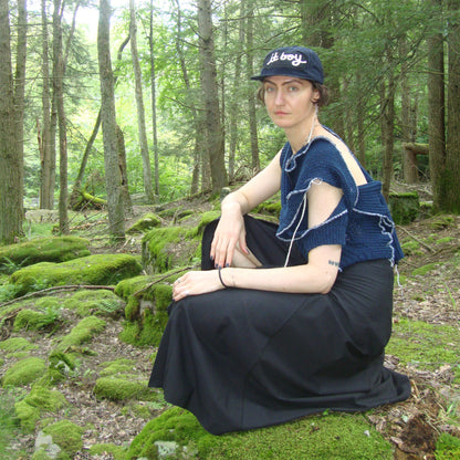 model posing in a mossy forest wearing navy blue baseball cap with copped brim and a black patch sewn over the front with white embroidered cursive reading it boy