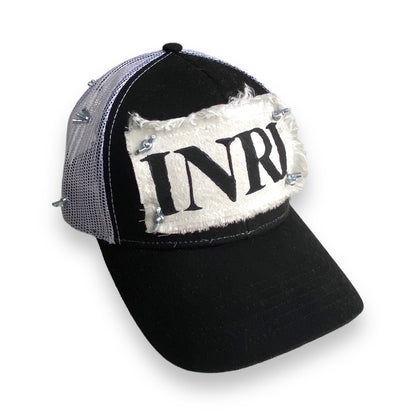 trucker hat with white mesh back, white patch with black INRI stamp, and nuts and bolts affixing the four corners of the patch to the front of the hat and wrapping around in a crown of thorns