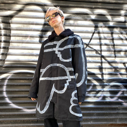 model posing wearing black long winter coat with faux shearling collar and white hand painted minimalist angel designs across the front and arms