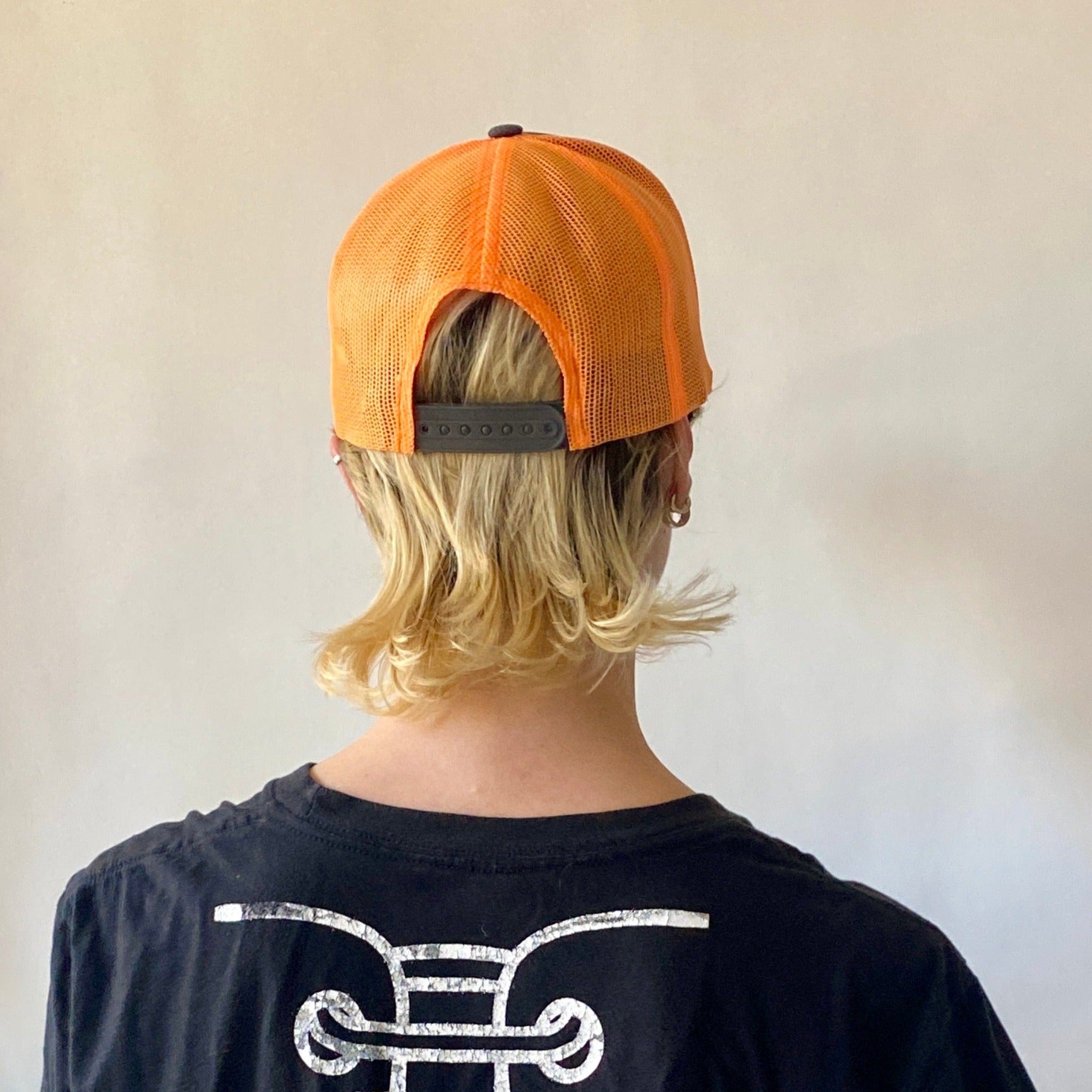 model facing away showing back of neon orange and stone gray trucker hat with adjustable snap back