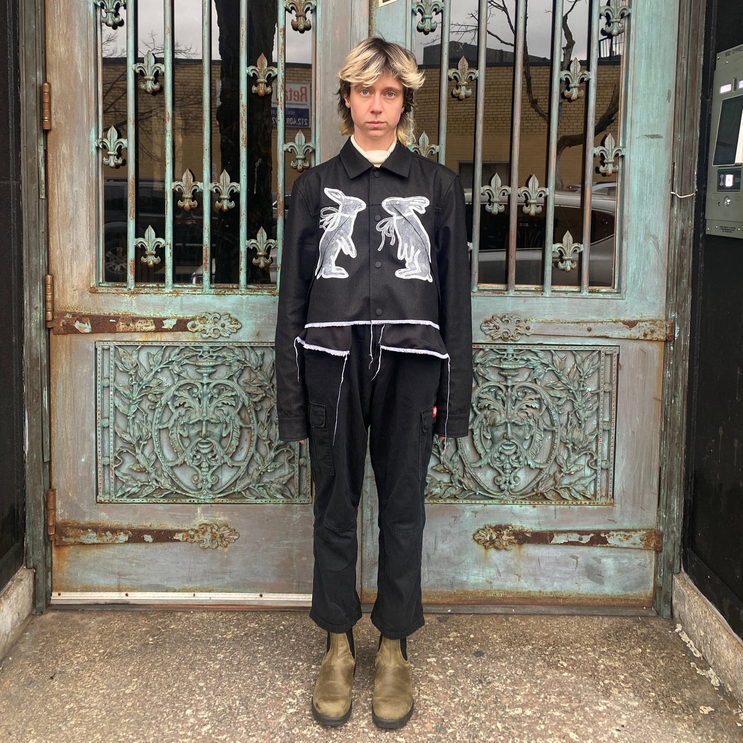 Model wearing white edged cropped black wool jacket hand-painted with two white rabbits with bows facing each other on the front