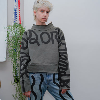 model posing wearing olive green mockneck with hand-painted cursive text across the arms and chest reading LOVERS OR FRIENDS