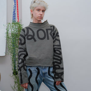 model posing wearing olive green mockneck with hand-painted cursive text across the arms and chest reading LOVERS OR FRIENDS