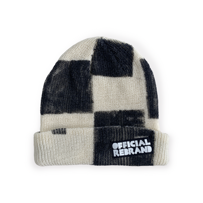 cream beanie with hand painted black checkered squares and a black tag with white text reading OFFICIAL REBRAND on the hat's cuff