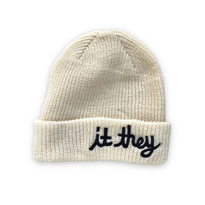white cream wool beanie with black cursive embroidery reading it they