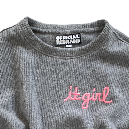 close up of neck and upper chest of gray knit sweater vest showing pink embroidery reading it girl and an inner black tag with white text reading OFFICIAL REBRAND