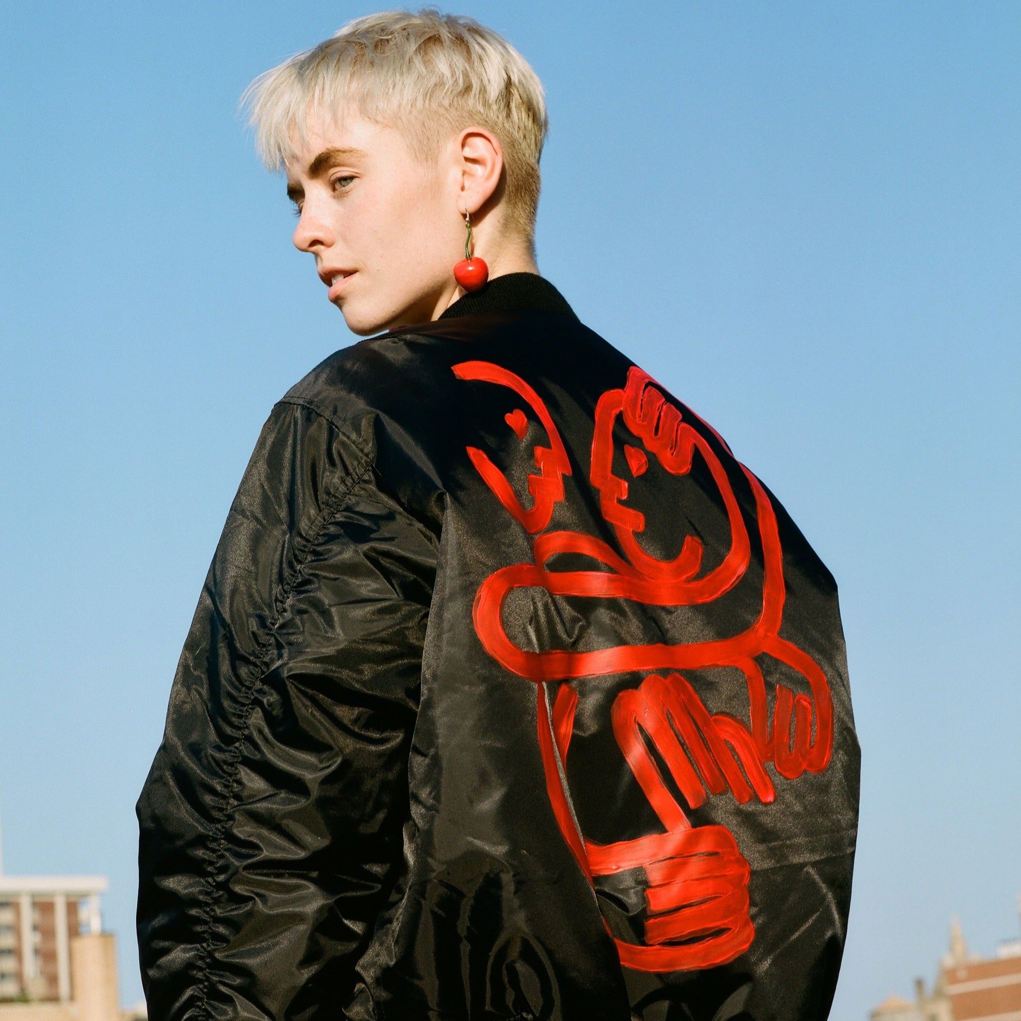 model facing away to show back of black bomber jacket with red hand-painted minimal design of two lovers embracing